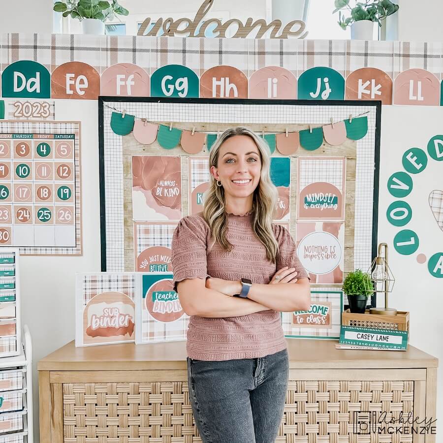 A woman standing in front of her modern plaid themed classroom bulletin board