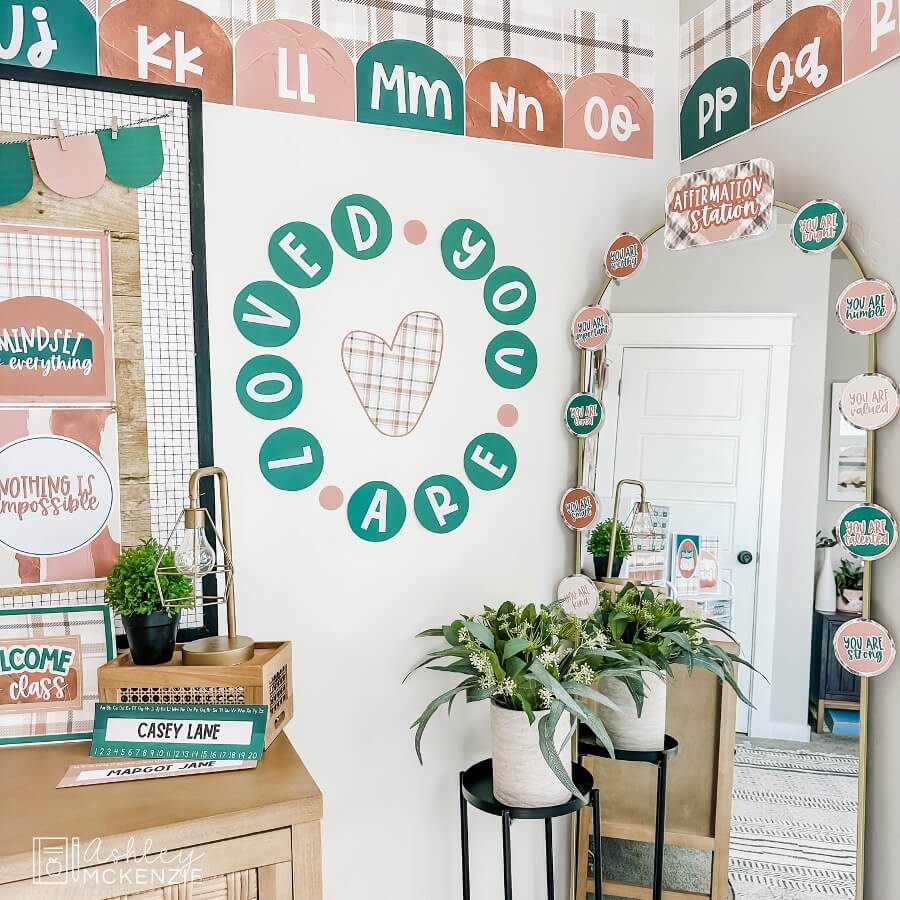 A classroom wall display with the saying "you are loved," and a full length mirror decorated with an affirmation station kit