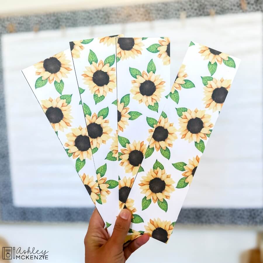 Several sections of a bulletin board border featuring a fall sunflowers decor theme are being held up to show the sunflower pattern up close.