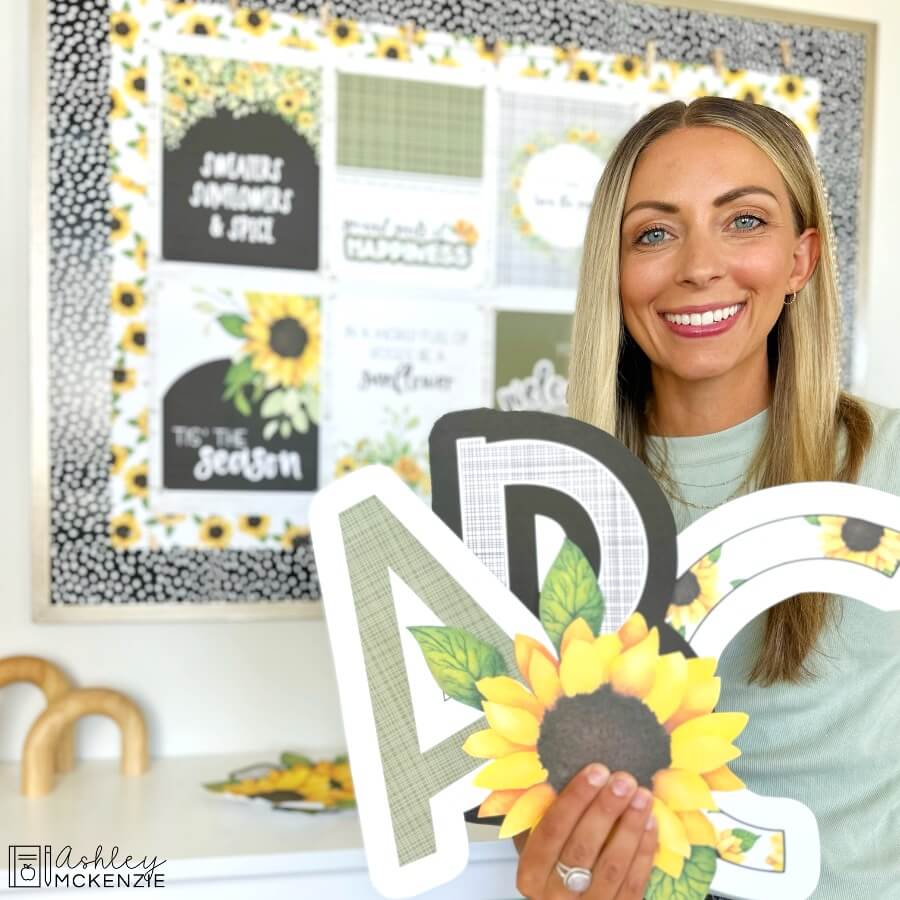 Cutouts of upper case letters A, B, and C, as well as a sunflower cutout are shown in front of a classroom bulletin board decorated with fall sunflowers themed classroom posters.