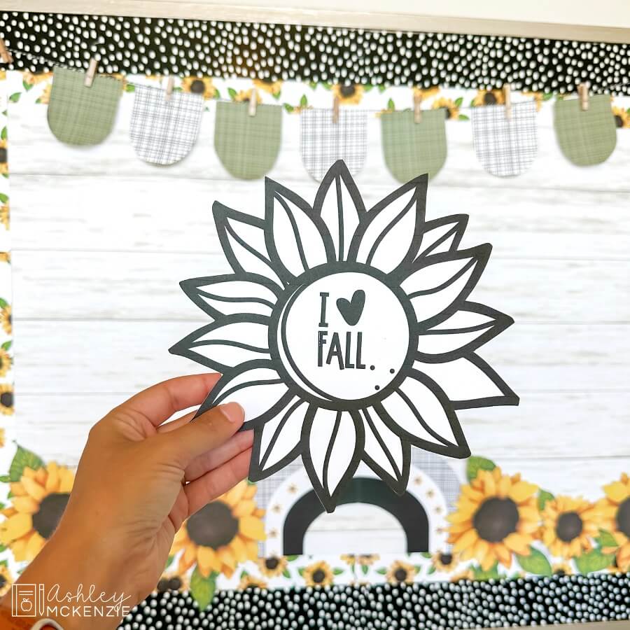 A hand holding up a sunflower template that has been cut out, and it says "I love fall" in the center of the flower.