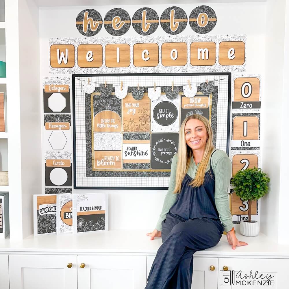 A teacher sitting in front of a classroom wall decorated with matching black and white classroom decor items