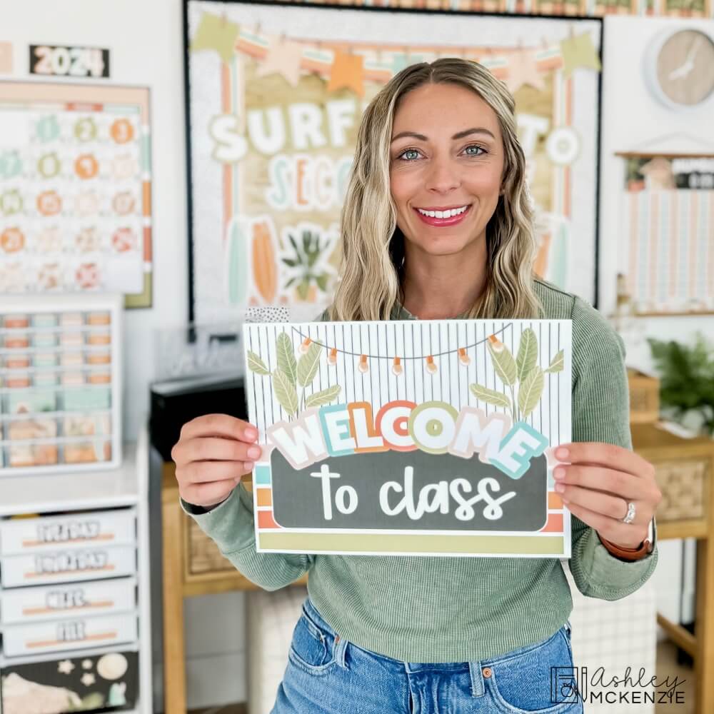 A teacher holding a free tropical themed sign that says "Welcome to class"