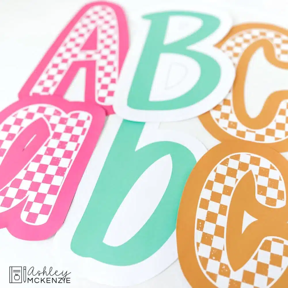 Bulletin board letters in a primary friendly font are shown featuring pink checkered pattern, solid turquoise, and a gold/yellow checkered pattern