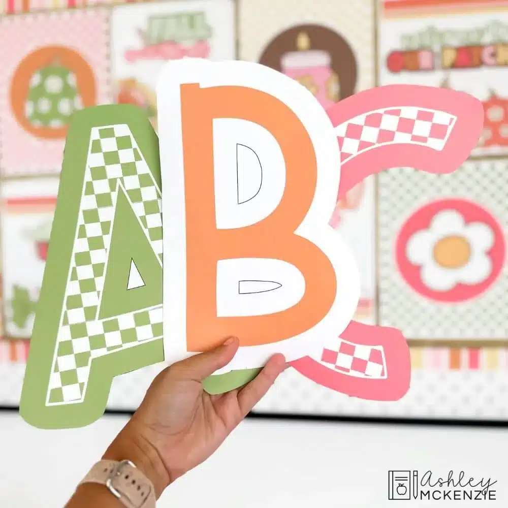 The letters A, B, and C are held up in a classroom as large, bulletin board letter cutouts in warm fall colors