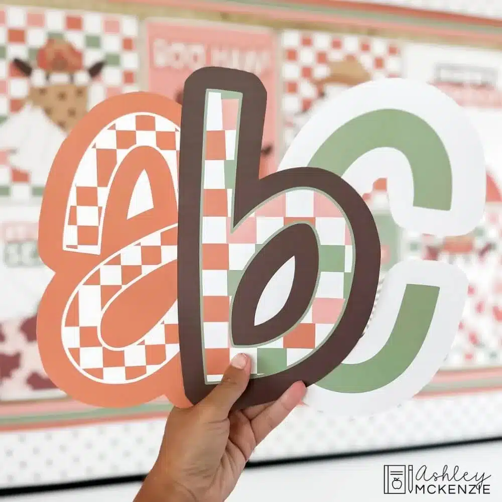 Checkered print bulletin board letters are held in front of a classroom bulletin board decorated for Halloween