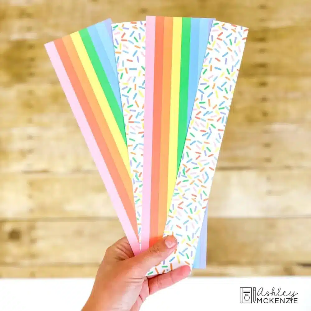 Colorful bulletin board borders are being held in front of a classroom bulletin board - the borders are rainbow stripes and colorful confetti designs.