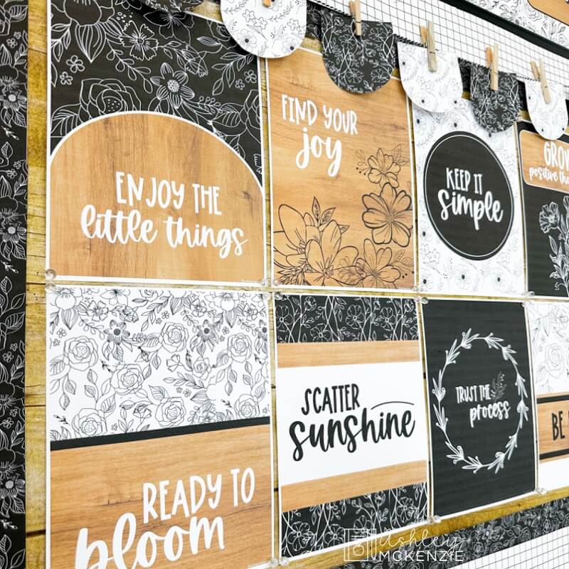 A bulletin board featuring posters in a black and white classroom decor design featuring floral accents and inspirational quotes