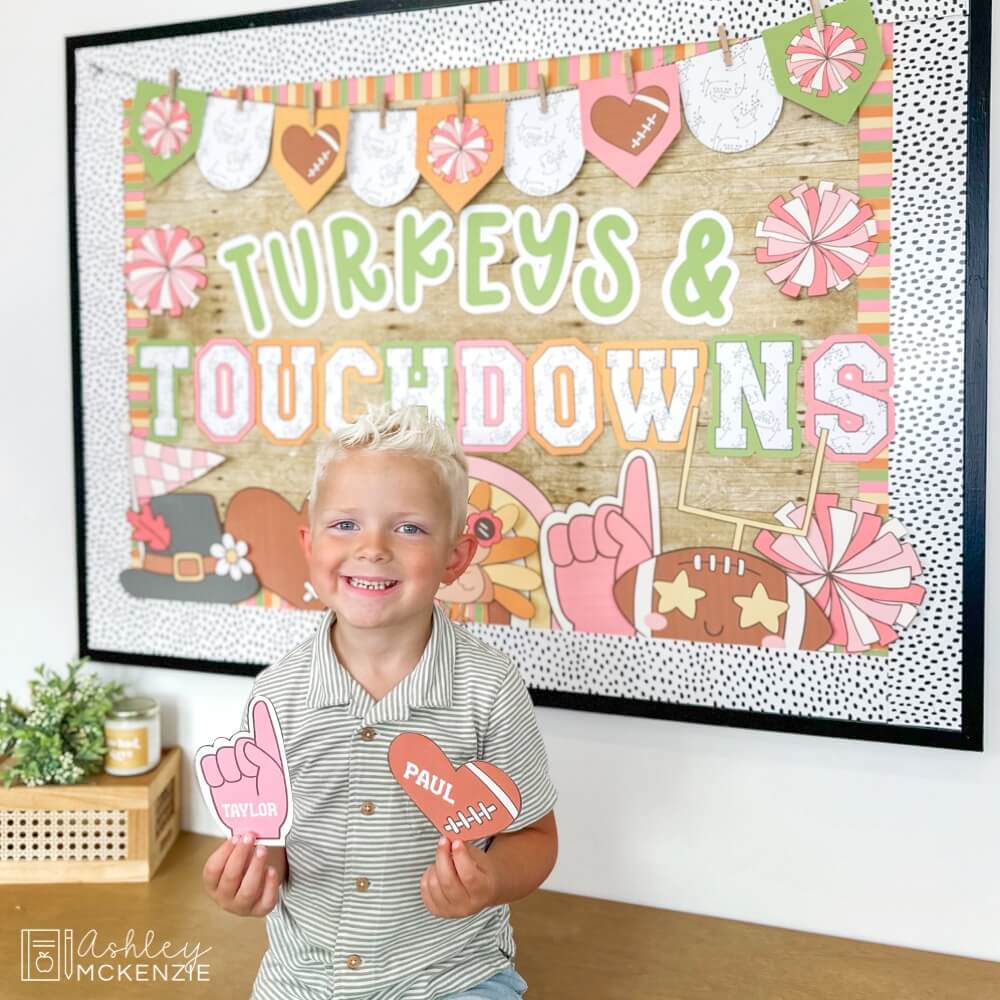 A Thanksgiving classroom display featuring a football bulletin board kit - a student stands in front of it holding little cutouts with student names printed on them