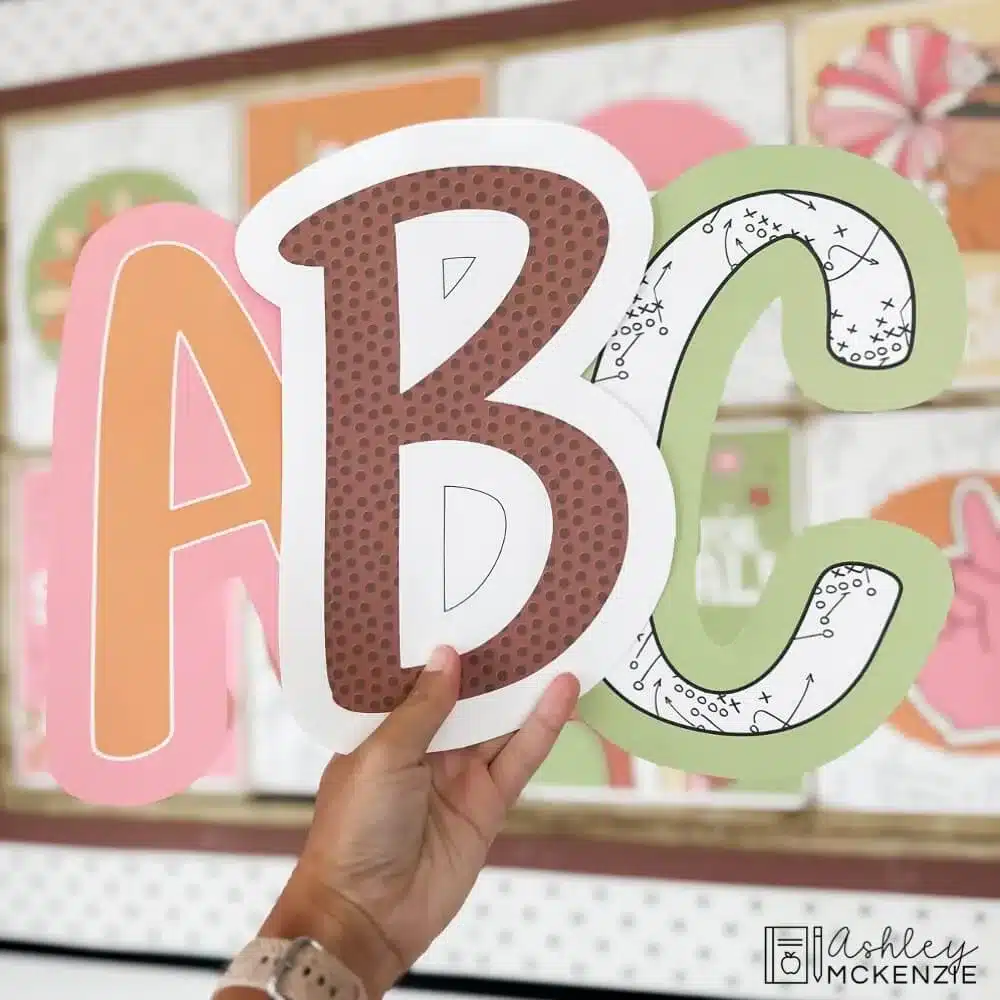 Thanksgiving and football themed bulletin board letters are shown in front of a classroom bulletin board in a primary friendly font