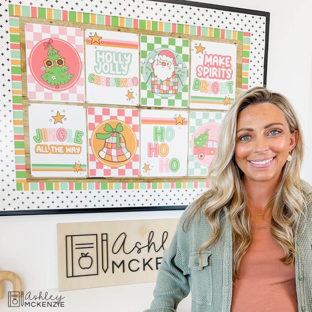 A teacher stands in front of a classroom bulletin board decorated for Christmas with holiday themed posters