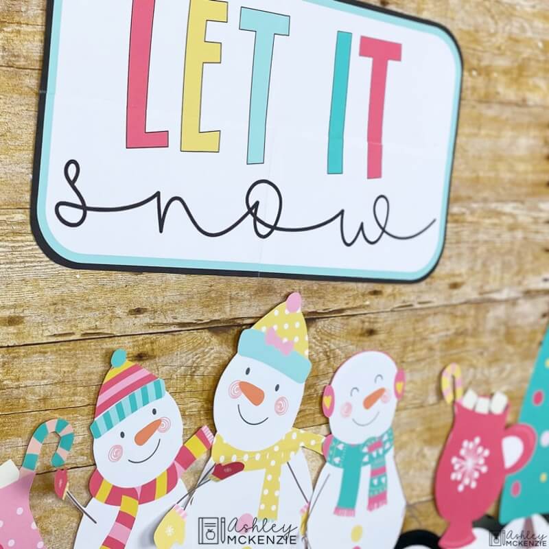 A closeup of a winter bulletin board idea featuring friendly snowmen, a large sign that says "Let it snow" and cutouts of hot cocoa mugs.