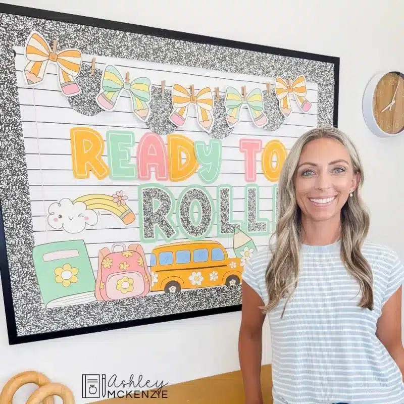 A teacher standing in front of a back to school bulletin board display featuring the saying "Ready to Roll"