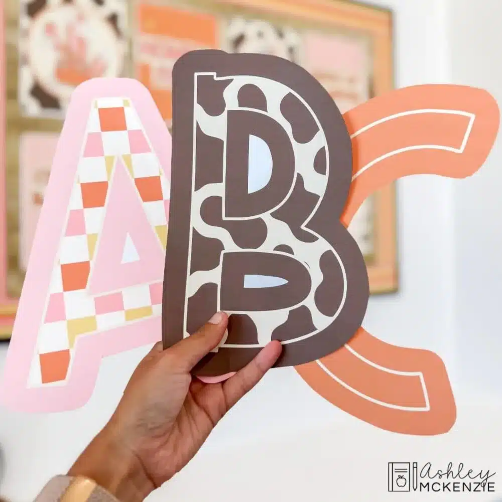 Fall bulletin board letters A, B, and C are held up featuring cow print, checkered patterns, and orange solid colors.